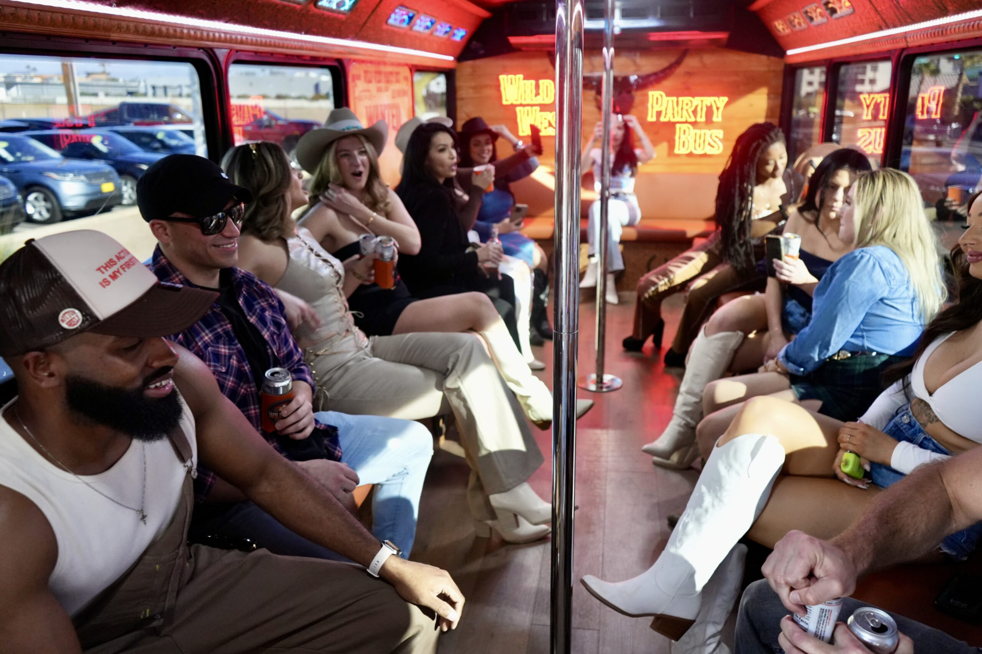 A full group seated along both sides of the bus interior under neon Wild West Party Bus signs