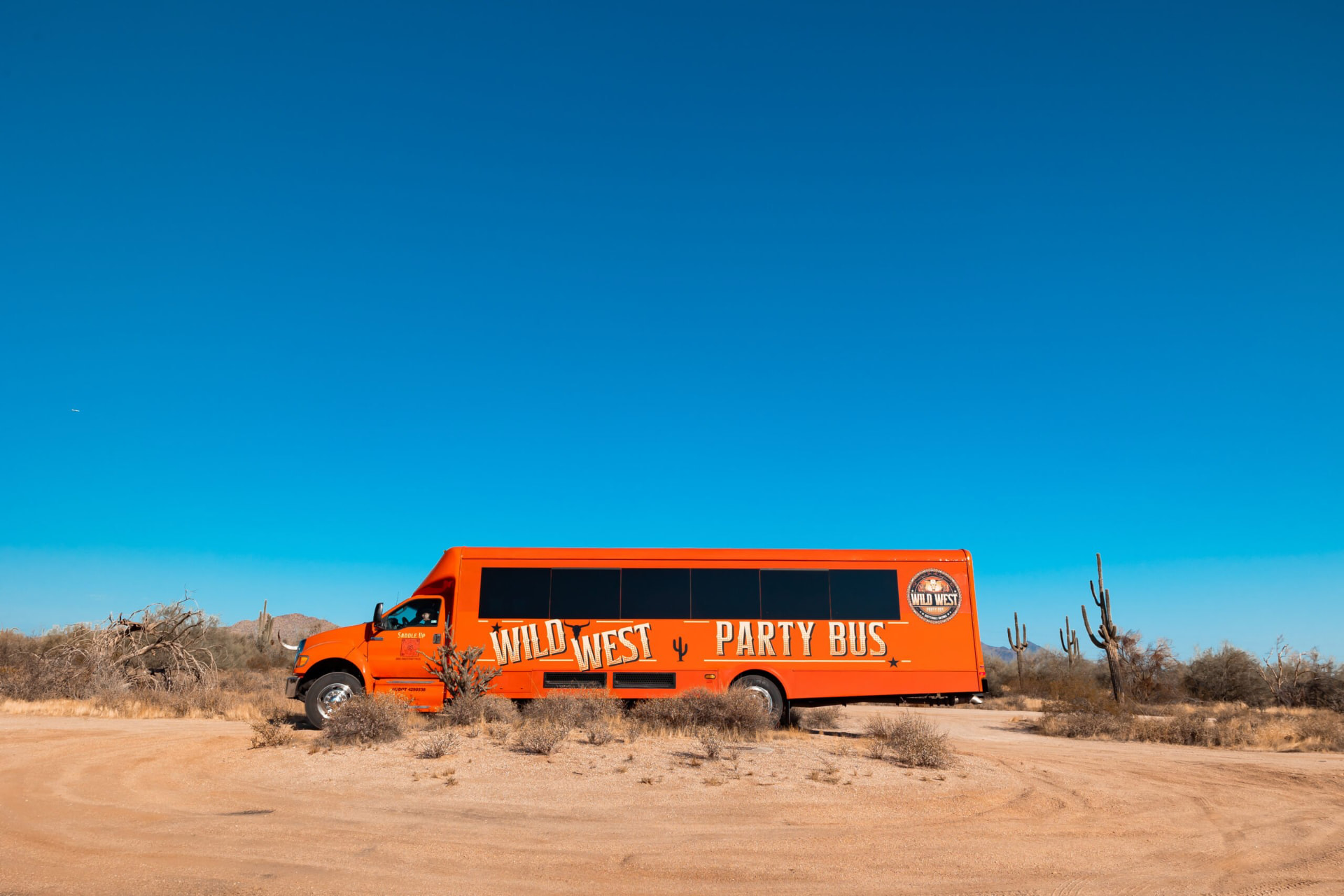 Side view of the orange Wild West Party Bus in the Sonoran desert showing its full length and branding