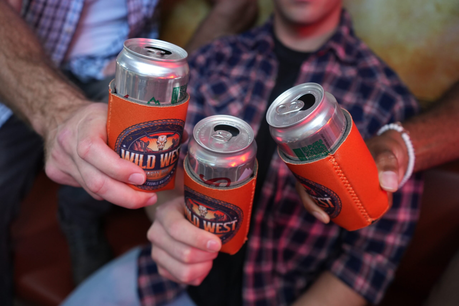 Guests toasting cans in orange Wild West Party Bus koozies on board