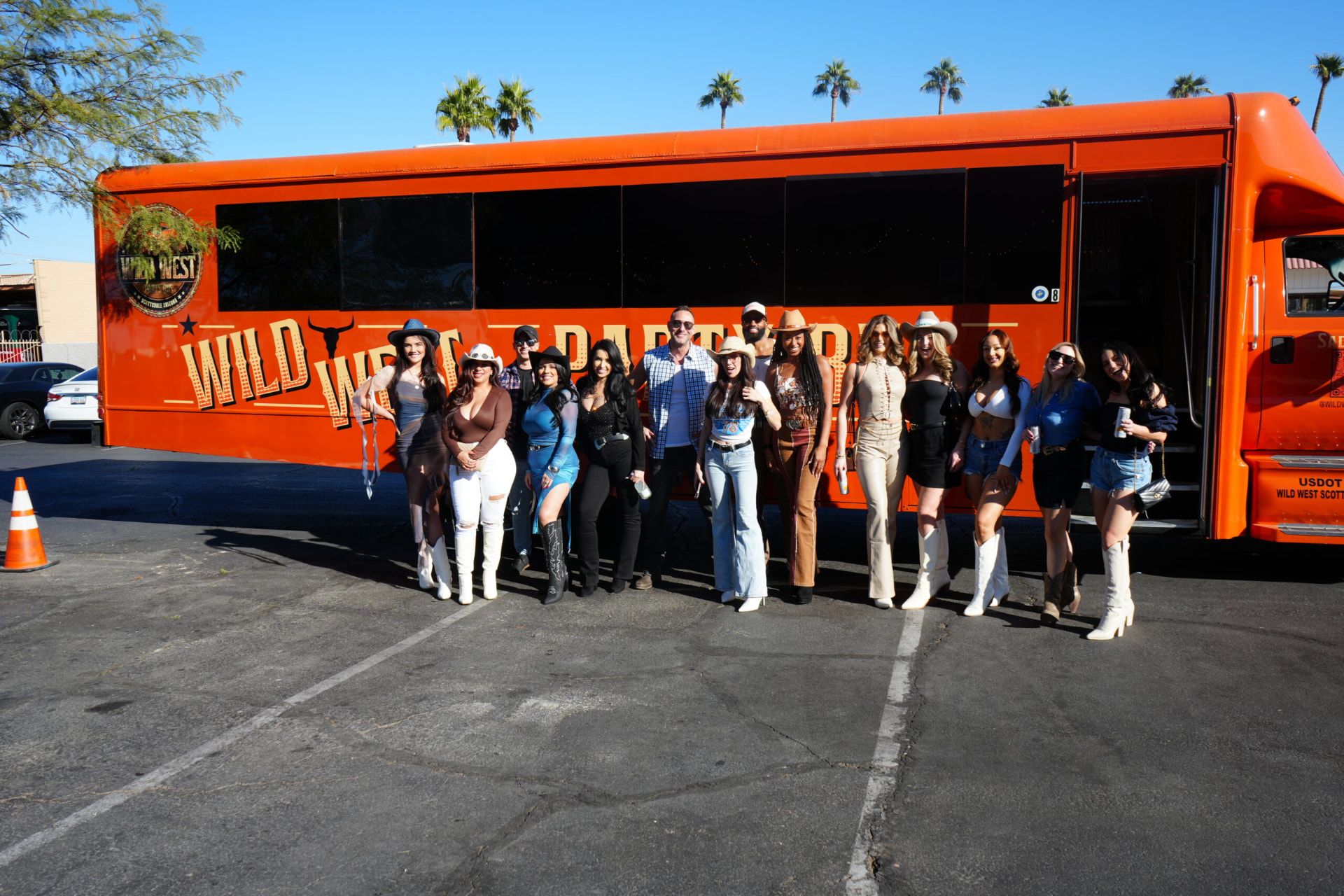 A large group posed alongside the orange Wild West Party Bus at a Scottsdale pickup